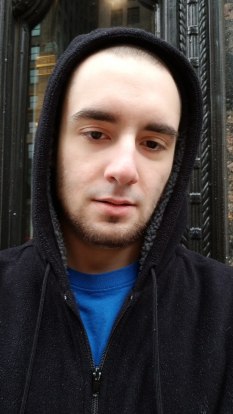 Jack Peterson, a white man with slight facial hair wearing a black hoodie with the hood up over a blue tee shirt.
